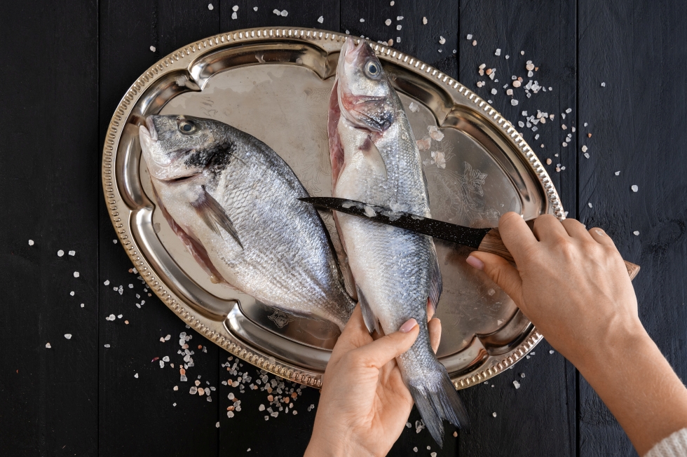 Две роскошные рыбки на красивом блюдце, которых режет человек ножом